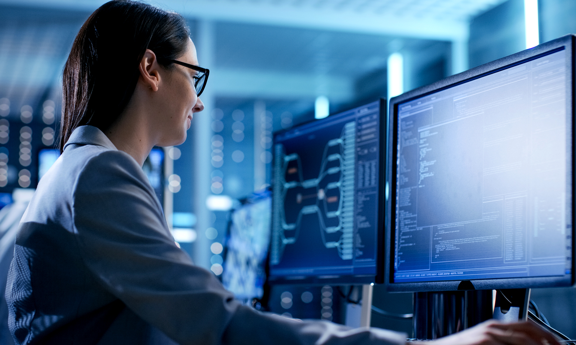 Close-up Shot of Female IT Engineer Working in Monitoring Room. She Works with Multiple Displays.